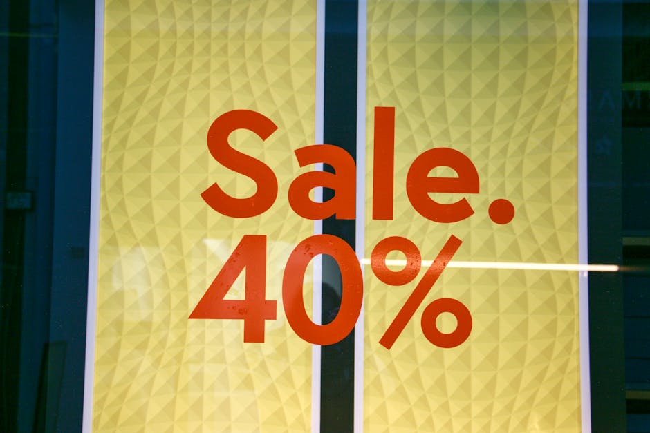 A promotional display window featuring bold red text reading 'Sale. 40%', set against a yellow background with a textured, geometric diamond pattern. The text is centrally positioned, with the word 'Sale.' at the top and the percentage discount just below. The background panels are framed by vertical white borders on either side, and the scene appears to be viewed through glass with a faint reflection visible across the surface. The environment suggests a retail setting, possibly in a shopping area or storefront, highlighting a discount offer that may relate to retail sales rather than waste management or rubbish clearance services. The image focuses solely on the sale sign without additional objects or contextual elements, providing a clear visual of promotional advertising.
